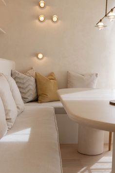 a white couch sitting next to a table in a living room with lights on the wall