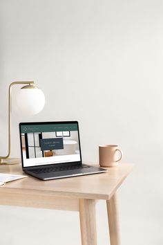 an open laptop computer sitting on top of a wooden desk next to a cup and lamp