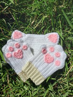 a crocheted mitt with pink flowers on it laying in the green grass