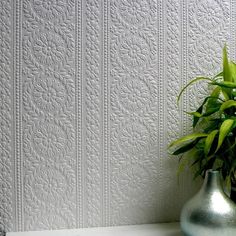 a green plant in a silver vase sitting on a shelf next to a white wall