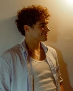 a young man with curly hair standing in front of a wall and looking off to the side