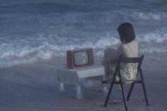 a woman sitting in a chair next to a tv on top of a table near the ocean