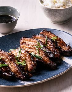 grilled pork chops on a blue plate with dipping sauce and rice in the background