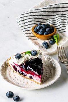 a slice of blueberry cheesecake on a plate with a fork and bowl of berries