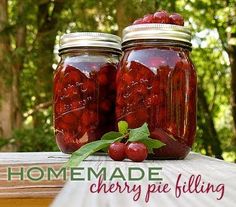 two jars filled with cherry pie filling sitting on top of a wooden table next to trees