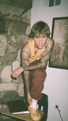 a man sitting on top of a skateboard in front of a stone wall with tattoos