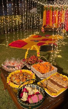 a table topped with lots of food on top of a lush green field covered in lights