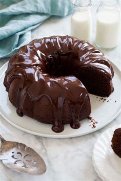 a chocolate bunt cake on a white plate next to some milk and spoons