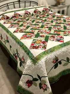 a bed with a quilted bedspread that has flowers and leaves on it