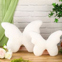 two white stuffed animals sitting on top of a wooden table next to flowers and greenery