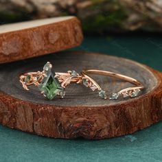 two rings with green stones sitting on top of a piece of wood