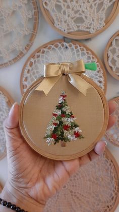 a hand holding a small christmas tree ornament in front of lace doily