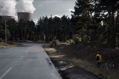 a man standing on the side of a road next to a forest filled with trees