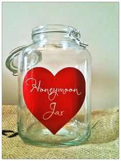 a glass jar with a red heart on the lid that says honeymoon jar in cursive writing