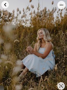 a woman is sitting in the grass with her hands together and looking at her phone