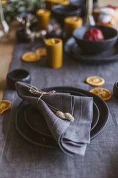 the table is set with black plates and napkins, silverware and orange slices