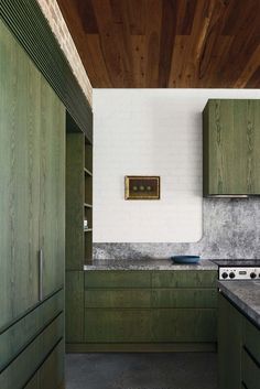 a kitchen with green cabinets and marble counter tops, along with wood paneling on the ceiling