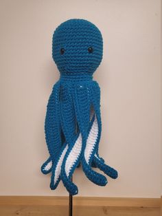 a crocheted blue octopus stuffed animal sitting on top of a wooden table next to a white wall