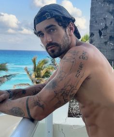 a man with tattoos on his arm leaning against a railing next to the ocean and palm trees