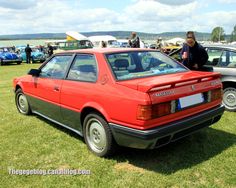 a red car parked on top of a lush green field next to other cars and people