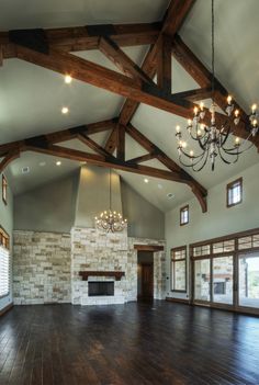 an empty living room with wood beams and chandelier hanging from the ceiling in front of a fireplace