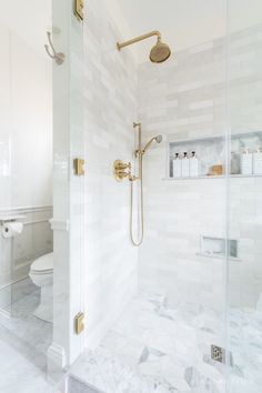 a white bathroom with gold fixtures and marble flooring on the walls, along with a walk in shower