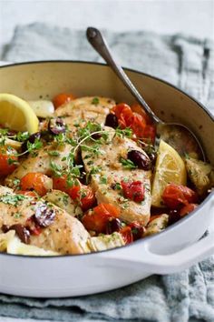 a pan filled with chicken and vegetables on top of a table next to a lemon wedge