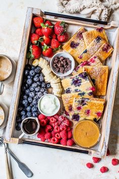 a wooden box filled with fruit and pastries on top of a white counter next to utensils