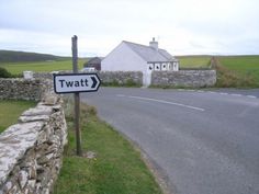 a street sign next to a stone wall with a white house in the back ground