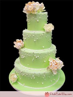 a three tiered green cake with flowers on the top and pearls on the bottom