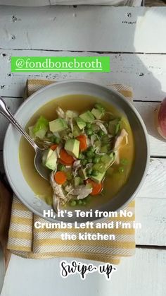 a white bowl filled with soup and vegetables on top of a wooden table next to an apple