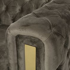 the back end of a grey velvet couch with gold trimmings and buttons on it