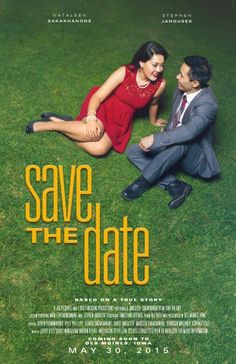 a man and woman sitting on the grass in front of a poster for save the date