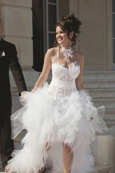 a woman in a white dress is walking down the street with another man wearing a tuxedo