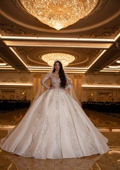 a woman in a wedding dress standing in a room with chandelier and lights