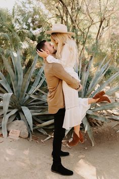 a man holding a woman in his arms while she is standing next to some plants