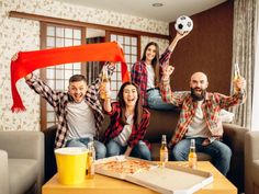 a group of people sitting on top of a couch holding up red scarfs in the air