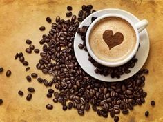 a cup of coffee with a heart in it surrounded by coffee beans on a table