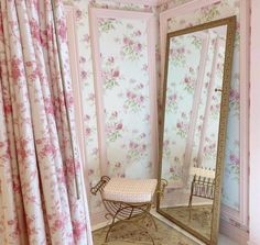 a room with a mirror, chair and wallpapered walls in the corner that has pink flowers on it