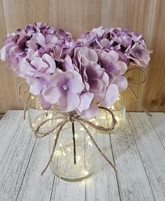 purple flowers are in a clear glass vase with string lights on the bottom and around it