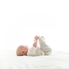 a baby laying on top of a bed with his hands in the air and looking up