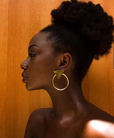 a woman wearing large gold hoop earrings with an earring on her left side, standing in front of a wooden wall