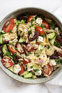 a bowl filled with pasta salad on top of a white table cloth next to a wooden spoon