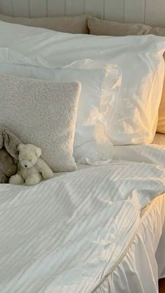 two teddy bears sitting on the edge of a bed with white linens and pillows