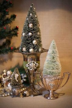 three small christmas trees sitting next to each other on top of silver cups and saucers