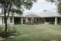 a white house sitting in the middle of a lush green field next to a tree