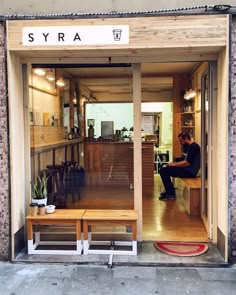 a man sitting on a wooden bench in front of a store window with the door open