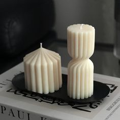 two white candles sitting on top of a black plate next to each other in front of a book