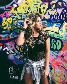 a beautiful young woman standing in front of a graffiti covered wall