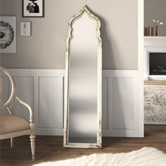 a large white mirror sitting on top of a wooden floor next to a chair and fireplace